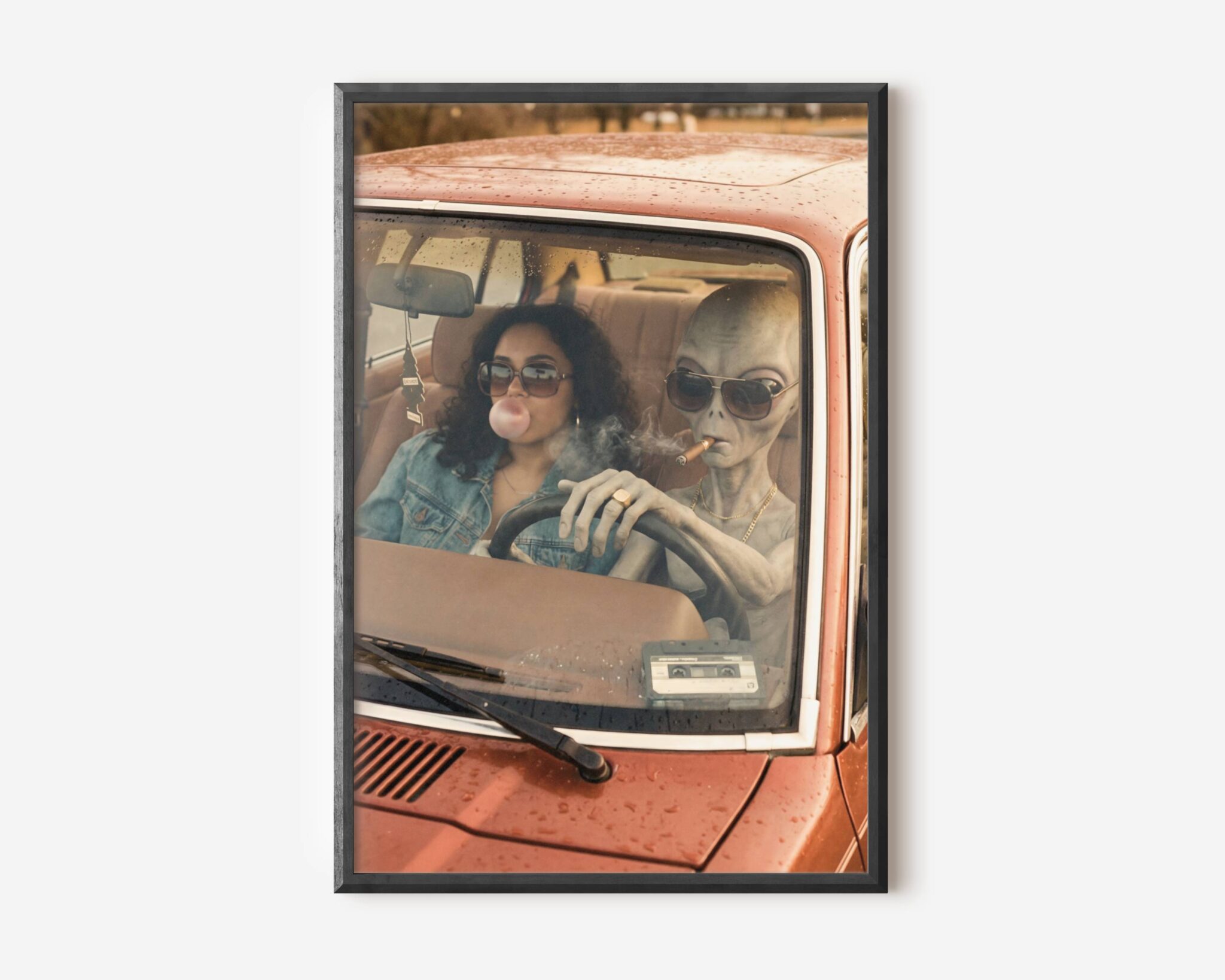 Premium retro sci-fi poster of a grey alien in gold chain and aviator sunglasses driving a battered vintage red car with a woman in denim blowing bubble gum, rain on the windscreen and a cassette tape on the dashboard – unframed alien art poster, ufoposter.com