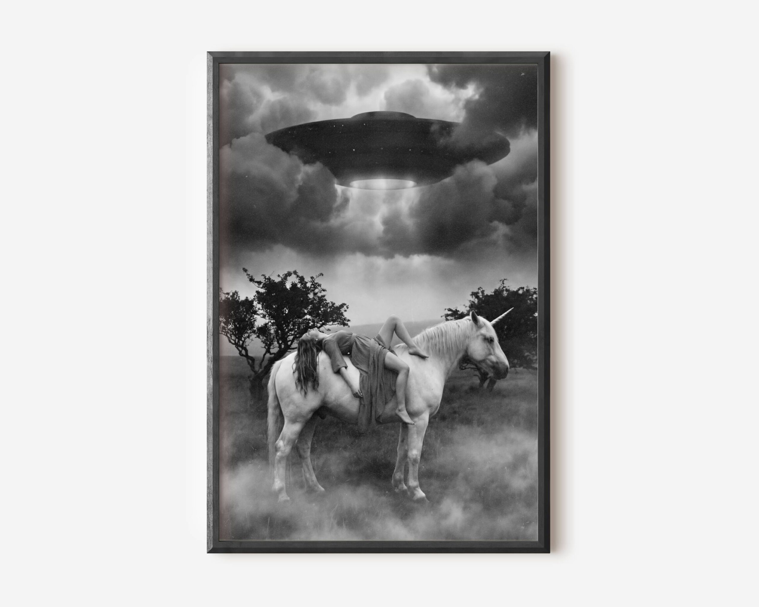 Black and white fine art print of a woman draped across the back of a white unicorn standing in a misty field, as a large UFO hovers above emitting a beam of light through dramatic storm clouds. A surreal and cinematic sci-fi wall art print printed on premium matte paper.