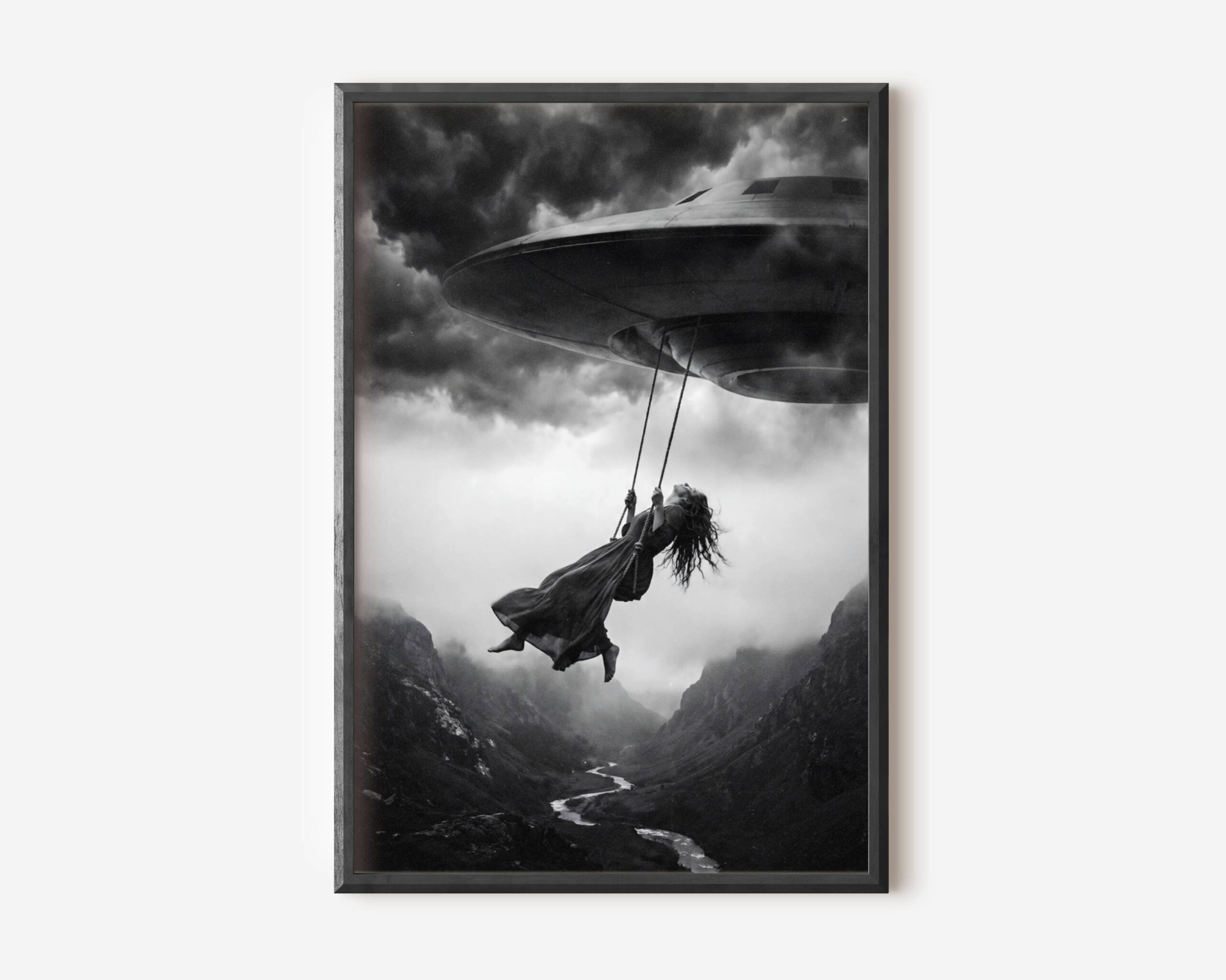 Black and white fine art print of a woman in a flowing dress swinging from a rope attached to a UFO spacecraft, suspended high above a dramatic mountain canyon under a stormy sky. A surreal and cinematic sci-fi wall art print printed on premium matte paper.