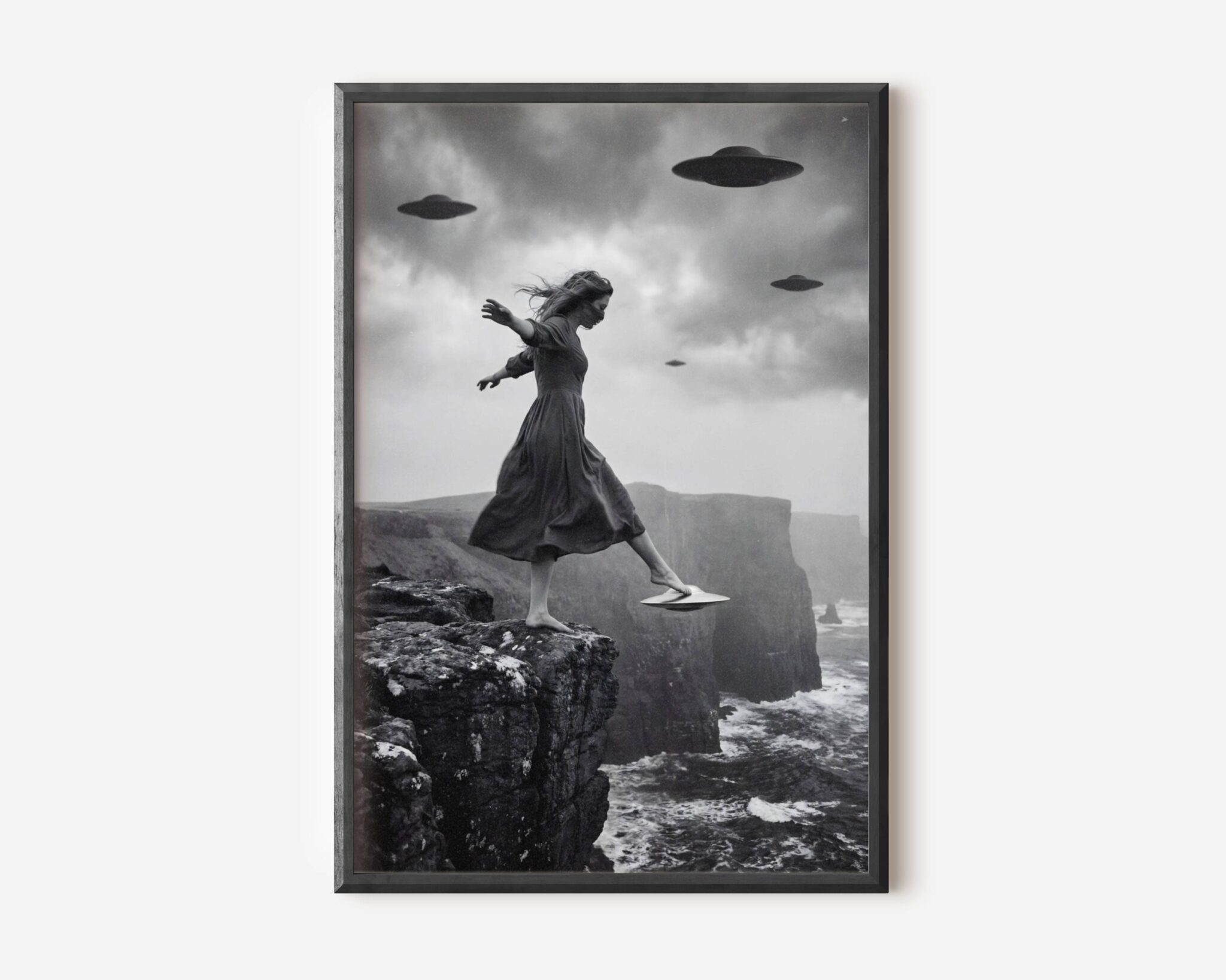 Black and white fine art print of a woman in a flowing dress stepping off the edge of a dramatic coastal cliff, one foot resting on a small hovering UFO, as three larger flying saucers circle in the stormy sky above crashing waves and towering sea cliffs. A surreal and cinematic sci-fi wall art print printed on premium matte paper.