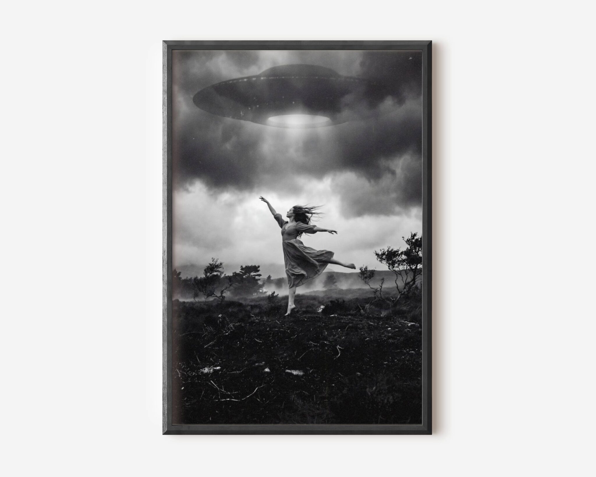 Black and white fine art print of a woman in a flowing dress dancing barefoot on a wild moorland, arms outstretched and one leg raised, as a large UFO hovers directly above her emitting a bright beam of light through dramatic storm clouds. A surreal and cinematic sci-fi wall art print printed on premium matte paper.