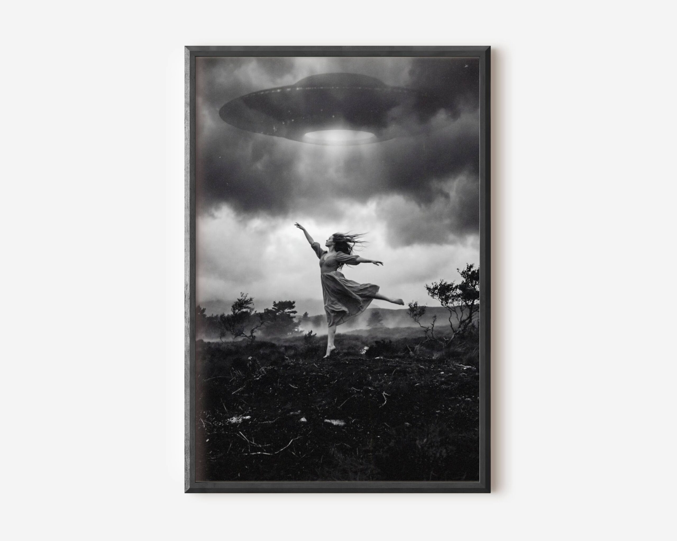 Black and white fine art print of a woman in a flowing dress dancing barefoot on a wild moorland, arms outstretched and one leg raised, as a large UFO hovers directly above her emitting a bright beam of light through dramatic storm clouds. A surreal and cinematic sci-fi wall art print printed on premium matte paper.