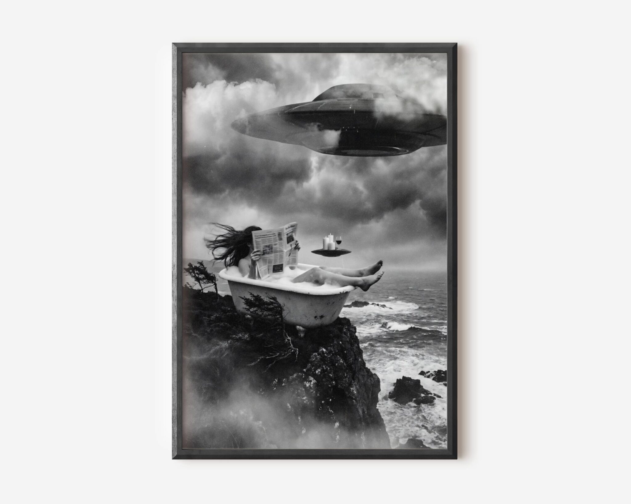 Black and white fine art print of a woman relaxing in a clawfoot bathtub perched on a rocky coastal cliff, reading a newspaper with complete composure as a massive UFO looms through storm clouds above her, while a small flying saucer hovers nearby serving as a tray for candles and a glass of wine. A surreal and darkly humorous cinematic sci-fi wall art print printed on premium matte paper.