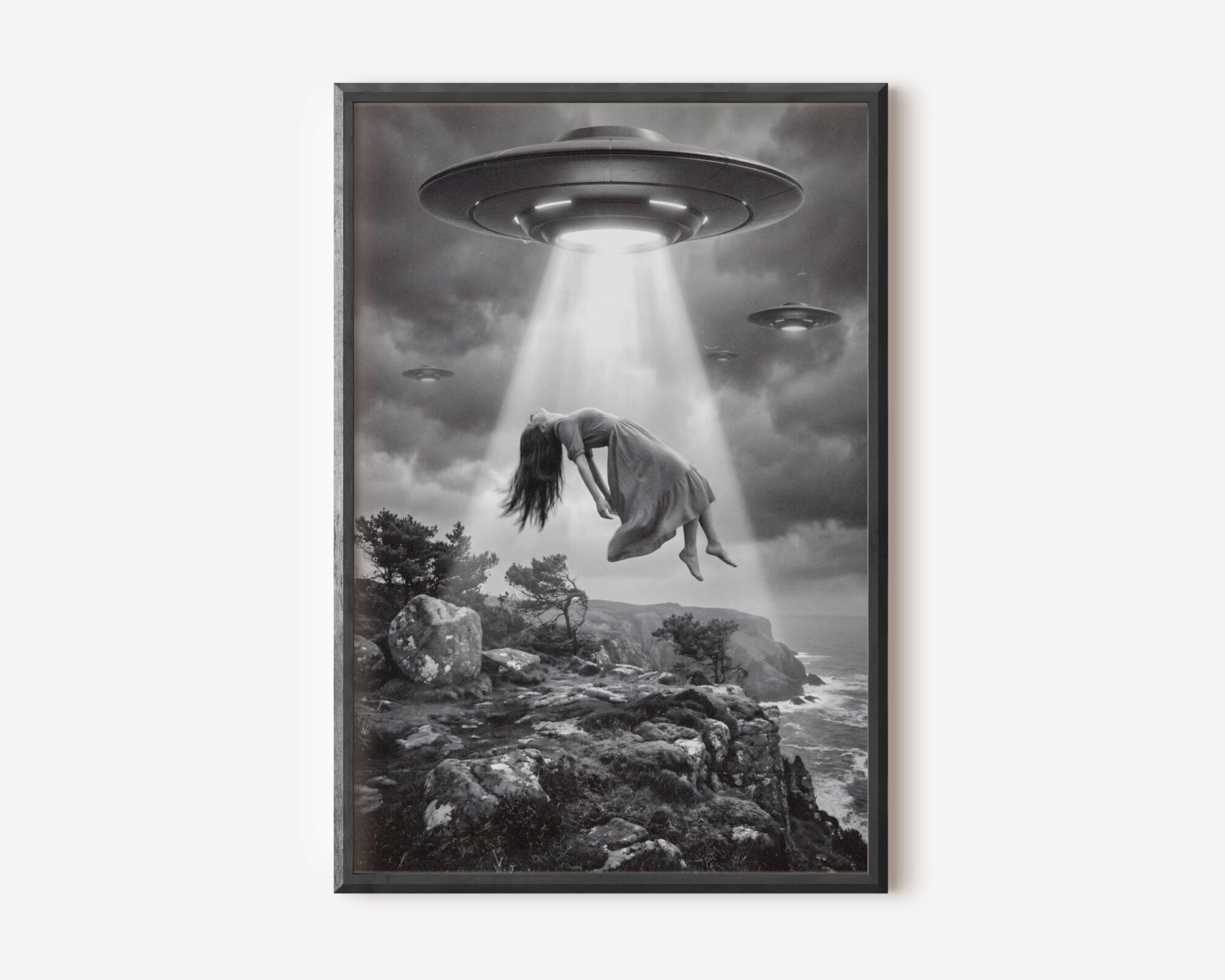 Premium dark surreal black and white poster of a woman floating weightlessly in a massive UFO beam above a dramatic rocky coastline, long hair streaming downward in quiet surrender as two more spacecraft drift through heavy storm clouds — hauntingly cinematic dark surreal wall art – unframed dark surreal art poster, ufoposter.com