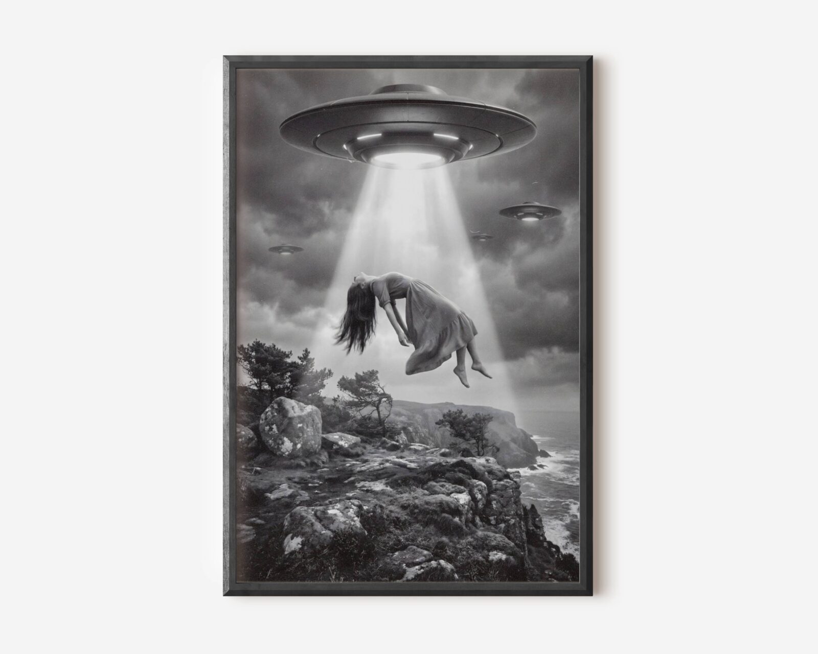 Premium dark surreal black and white poster of a woman floating weightlessly in a massive UFO beam above a dramatic rocky coastline, long hair streaming downward in quiet surrender as two more spacecraft drift through heavy storm clouds — hauntingly cinematic dark surreal wall art – unframed dark surreal art poster, ufoposter.com