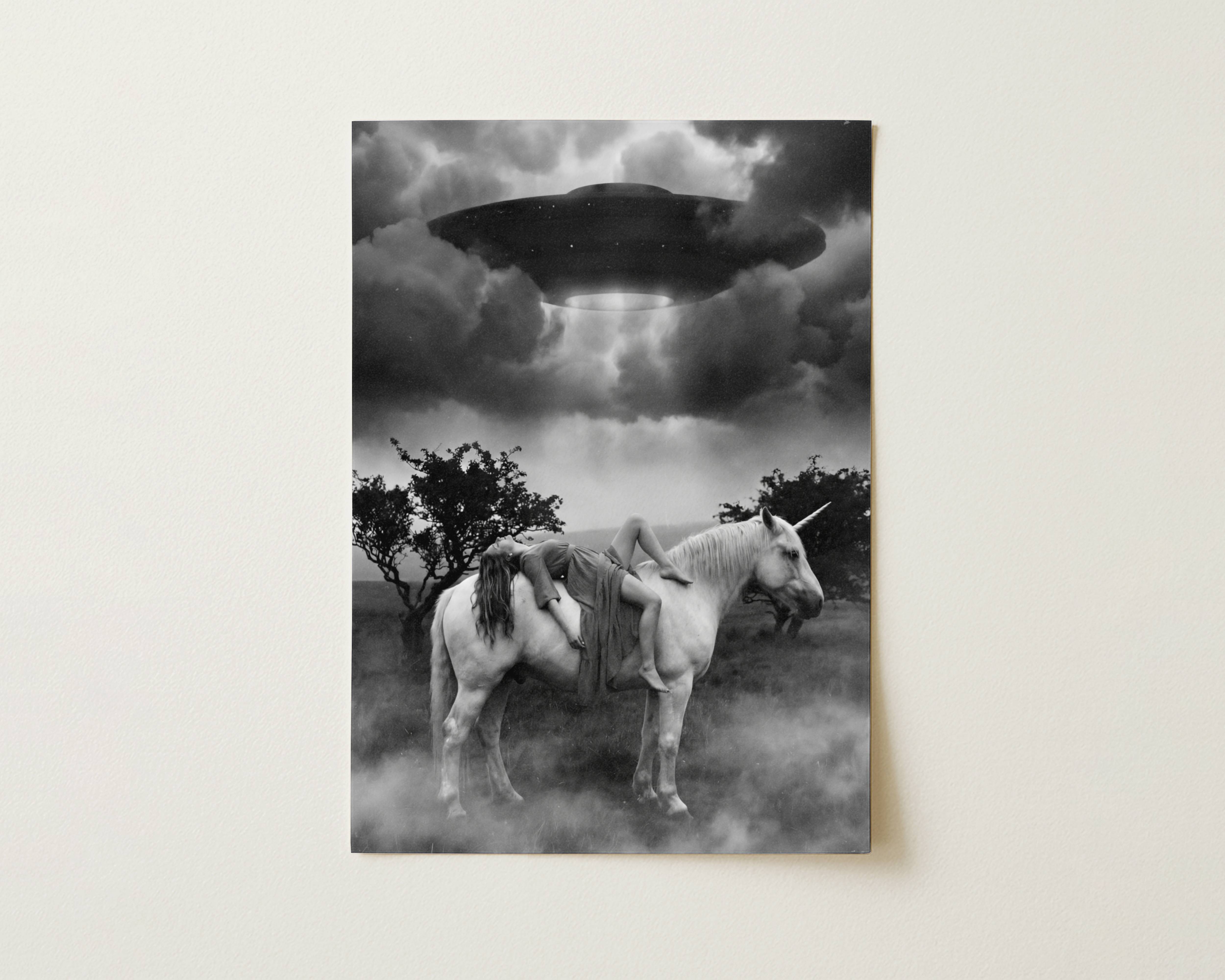Black and white fine art print photographed flat as a sheet of paper, showing a woman lying across a white unicorn in a foggy landscape with dark trees on either side and a massive UFO beaming light down from a stormy sky above. The flat lay highlights the rich tonal contrast and fine detail of this surreal cinematic art poster.