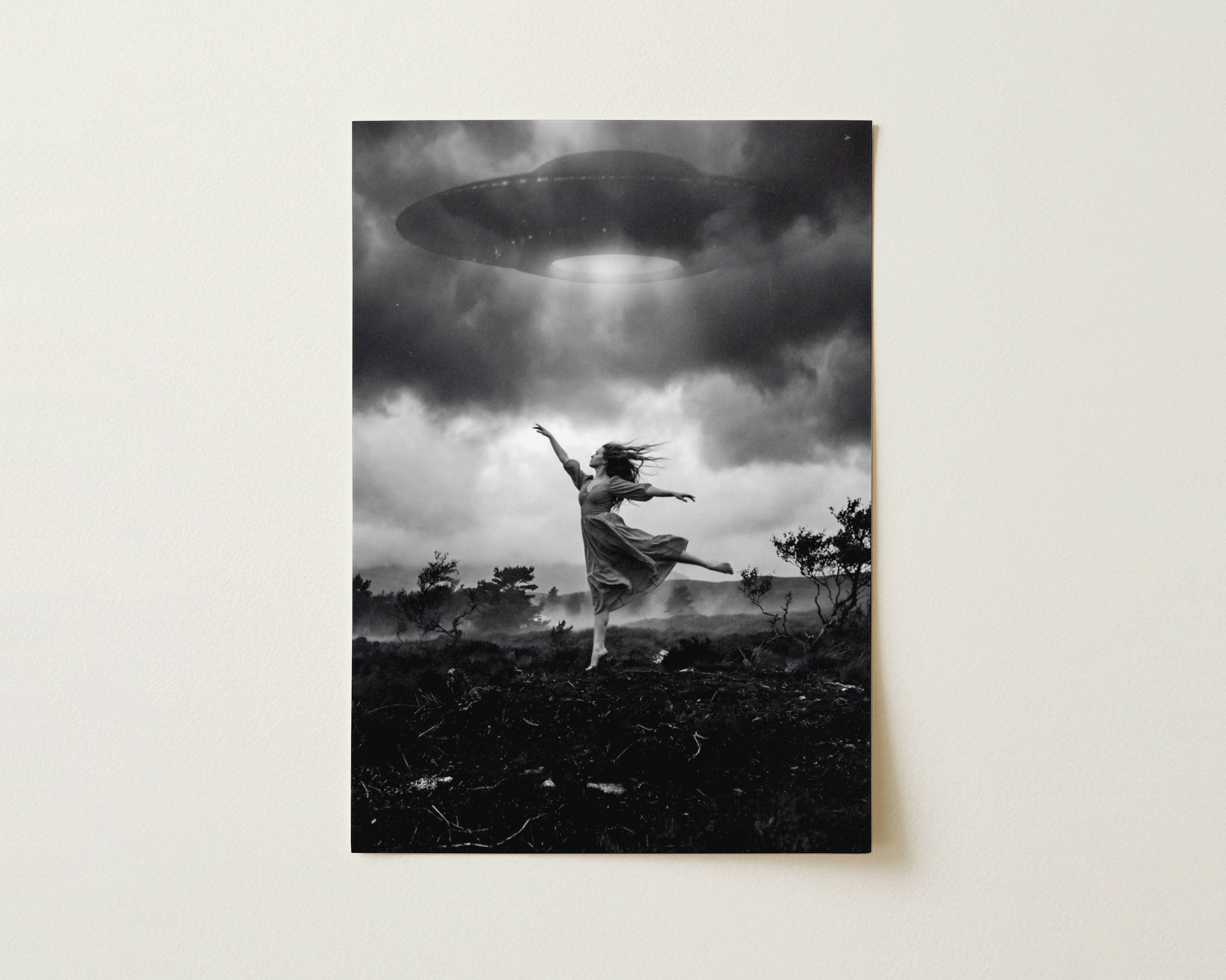 Black and white fine art print photographed flat as a sheet of paper, showing a barefoot woman dancing on a dark moorland with arms spread wide beneath a massive UFO beaming light down from a stormy sky. The flat lay highlights the rich tonal contrast and fine detail of this surreal cinematic art poster.
