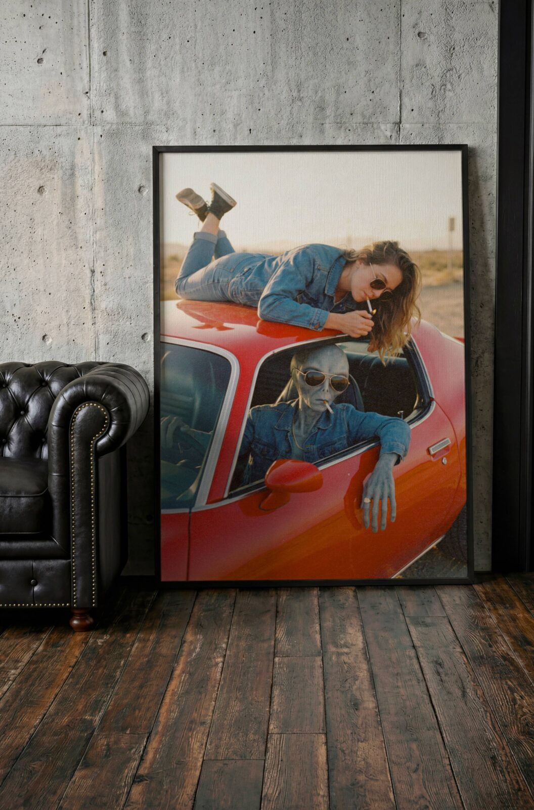 Lifestyle retro artwork of a cool grey alien and a carefree woman in matching denim sharing a cigarette moment on a classic red car against a warm golden desert backdrop – unframed alien lifestyle wall poster, ufoposter.com