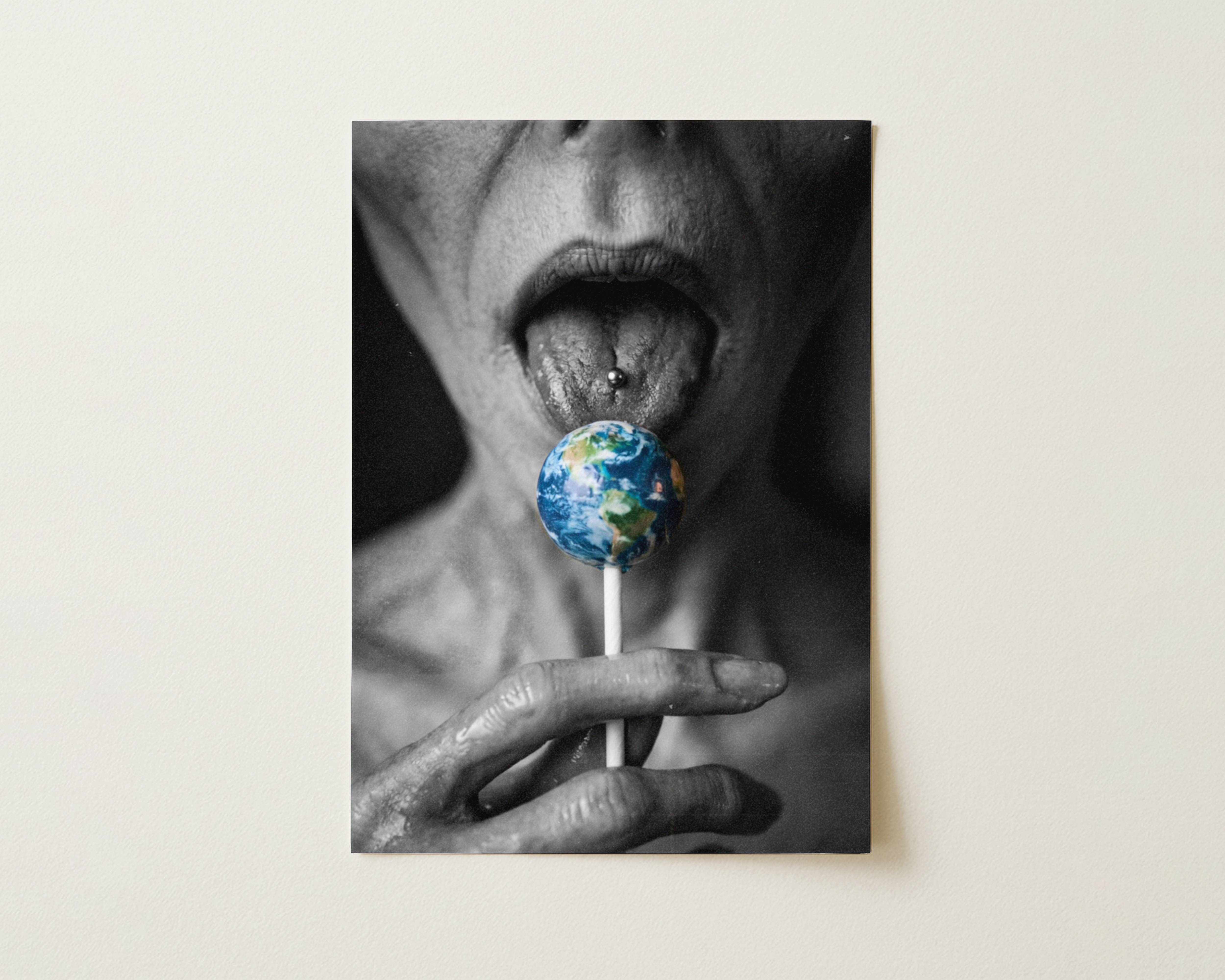 Black and white flat print close-up of a grey alien licking an Earth-shaped lollipop with a pierced tongue – high quality unframed flat poster print, ufoposter.com