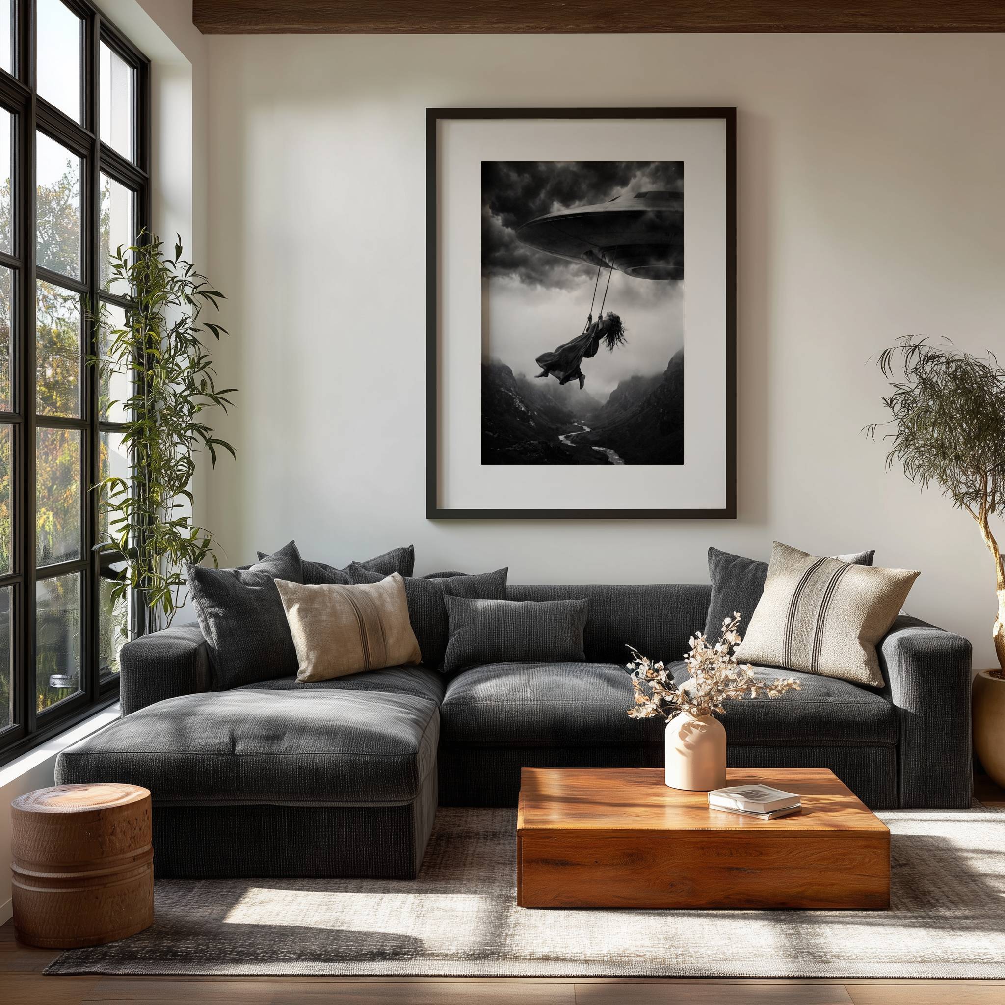 Black and white surreal art print of a woman swinging from a UFO above a dramatic mountain landscape, displayed on a living room wall, bringing cinematic tension and imaginative fine art energy to a modern interior.