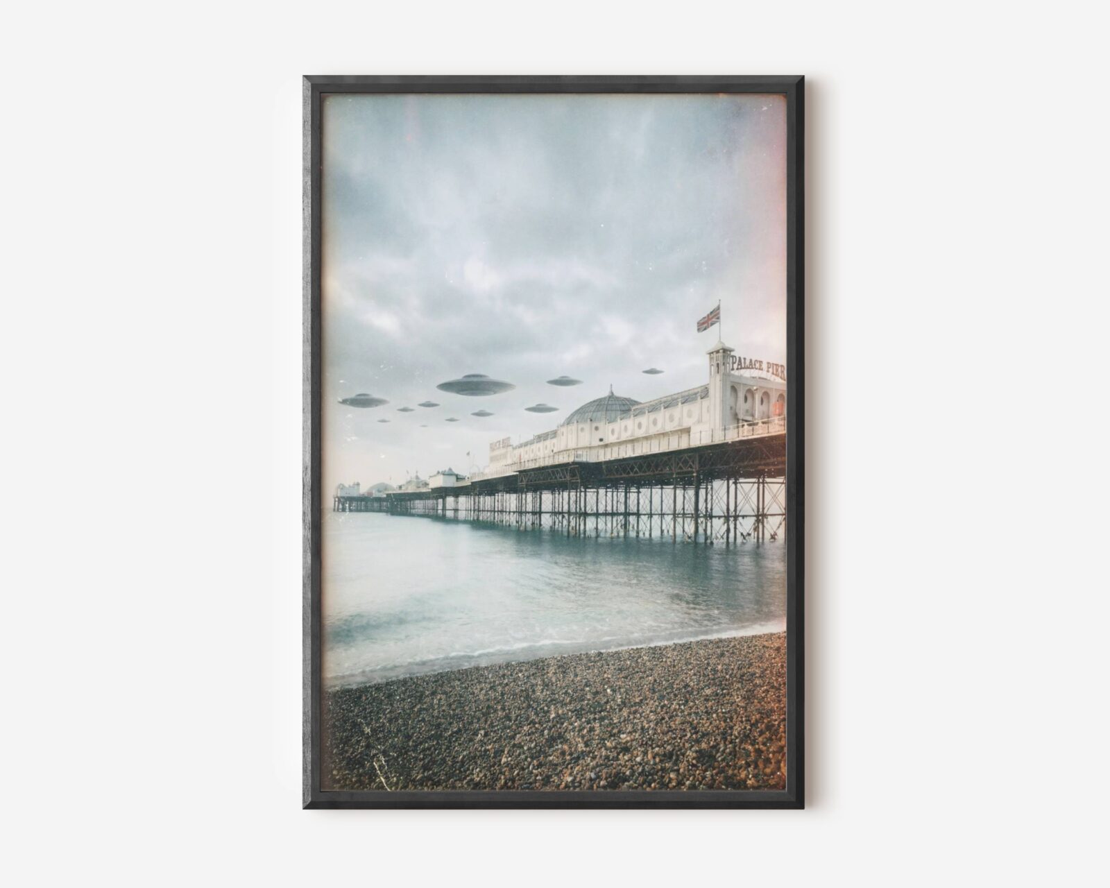 Premium soft retro sci-fi poster of a fleet of UFOs hovering in perfect formation above Brighton Palace Pier in a pale grey winter sky, Union Jack flying from the tower and the shingle beach and calm grey-green sea stretching below — a beautifully atmospheric and uniquely British UFO wall art print – unframed retro Brighton alien art poster, ufoposter.com