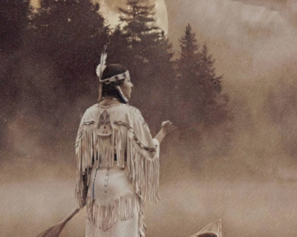 Intimate warm sepia close-up of a Native American woman in traditional fringed dress standing in a wooden canoe on a still misty lake, one hand raised toward the amber sky as a full moon glows above dark pines and a UFO drifts silently through the mist – unframed sepia UFO detail poster, ufoposter.com