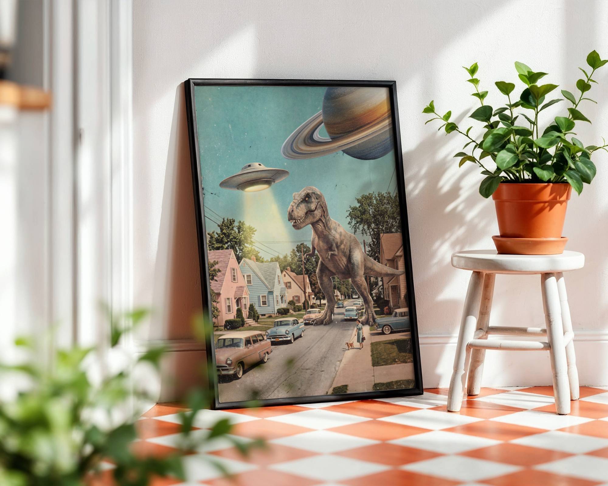 Bright pastel retro collage of a giant T-Rex striding down a 1950s American suburban street past vintage cars and pastel houses while a UFO hovers overhead and Saturn looms in the sky — bold and brilliant funny retro kitchen wall art print – unframed funny retro poster for kitchen, ufoposter.com